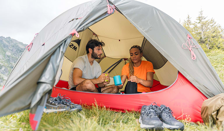Man and Woman sitting in a tent drinking from mugs wearing Merino Tech Lite II Short Sleeve Tee first layers in Flash and Ether