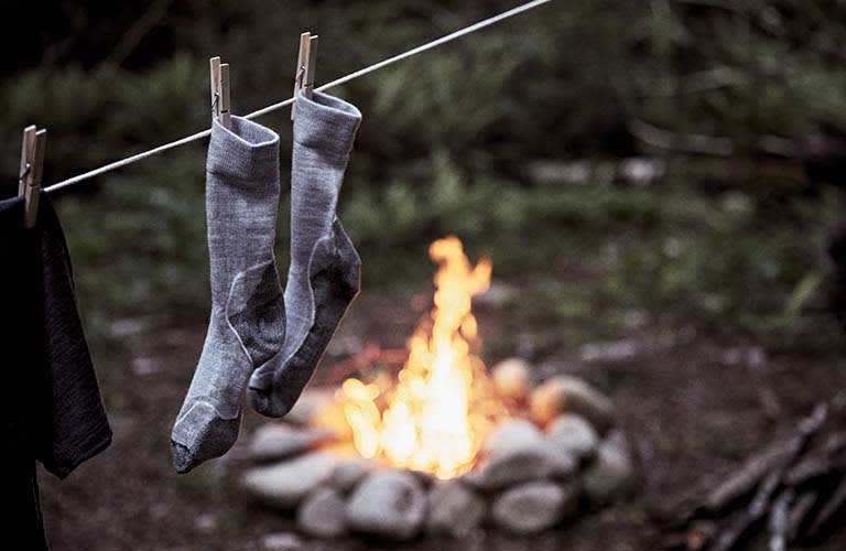 chaussettes en laine mérinos icebreaker accrochées à une corde à linge devant un feu