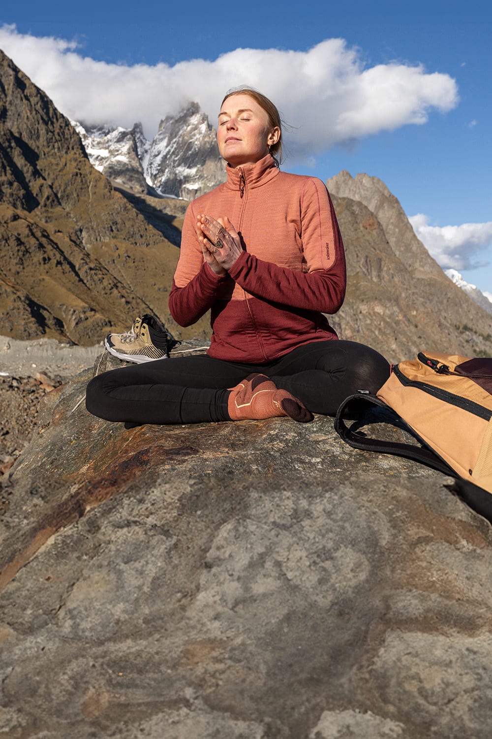 Woman sitting in the mountains wearing icebreaker clothing and doing meditation. Image focus is on her orange red icebreaker socks.