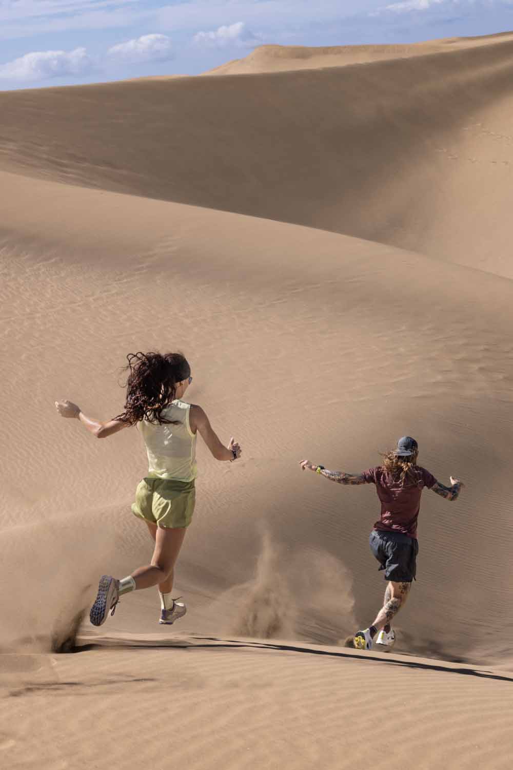 Man and woman running down sand dune wearing icebreaker featherlight merino t-shirt and featherlight merino tank