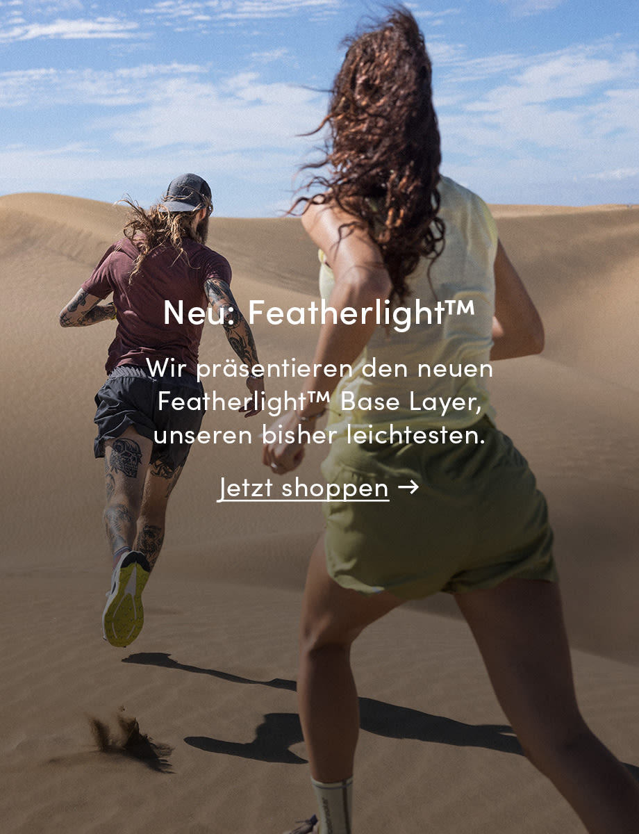 Two people running in icebreaker featherlight in the sand. The text on the image reads: New: Featherlight. Introducing the new Featherlight base layer, our lightest yet. Click on the image to shop now.