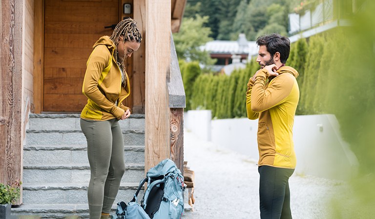 Man and woman zipping up merino hooded sweater with hiking pack