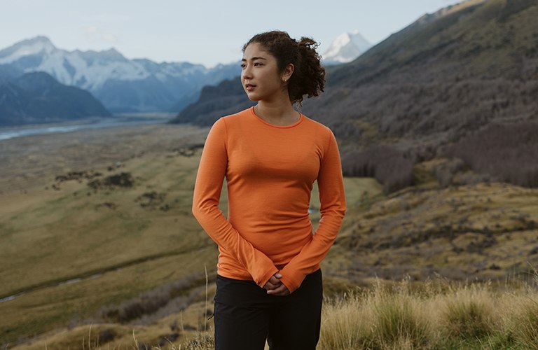 Woman hiking wearing an flash orange merino base layer thermal top