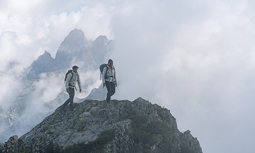 Man and woman ontop of rocky mountain wearing icebreaker merino realfleece high pile jackets and wearing hiking packs