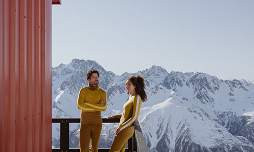 Woman and man standing at ski hut wearing icebreaker zoneknit thermal merino top and leggings