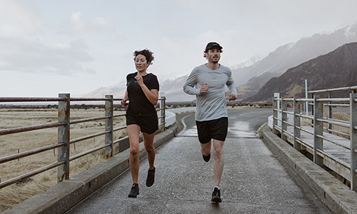 Man and woman running across a bridge wearing icebreaker merino zoneknit t-shirts and shorts