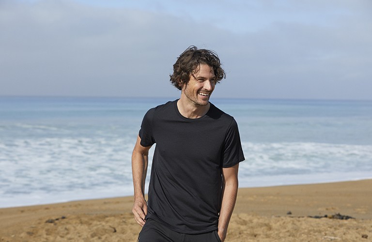Homme debout sur la plage portant un t-shirt mérinos noir icebreaker