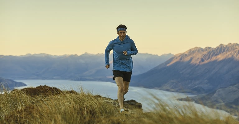 Man running up a hill wearing icebreaker merino running socks, shorts and long sleeve top