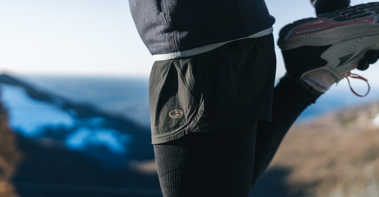 Man stretching wearing icebreaker merino running socks, shorts and leggings