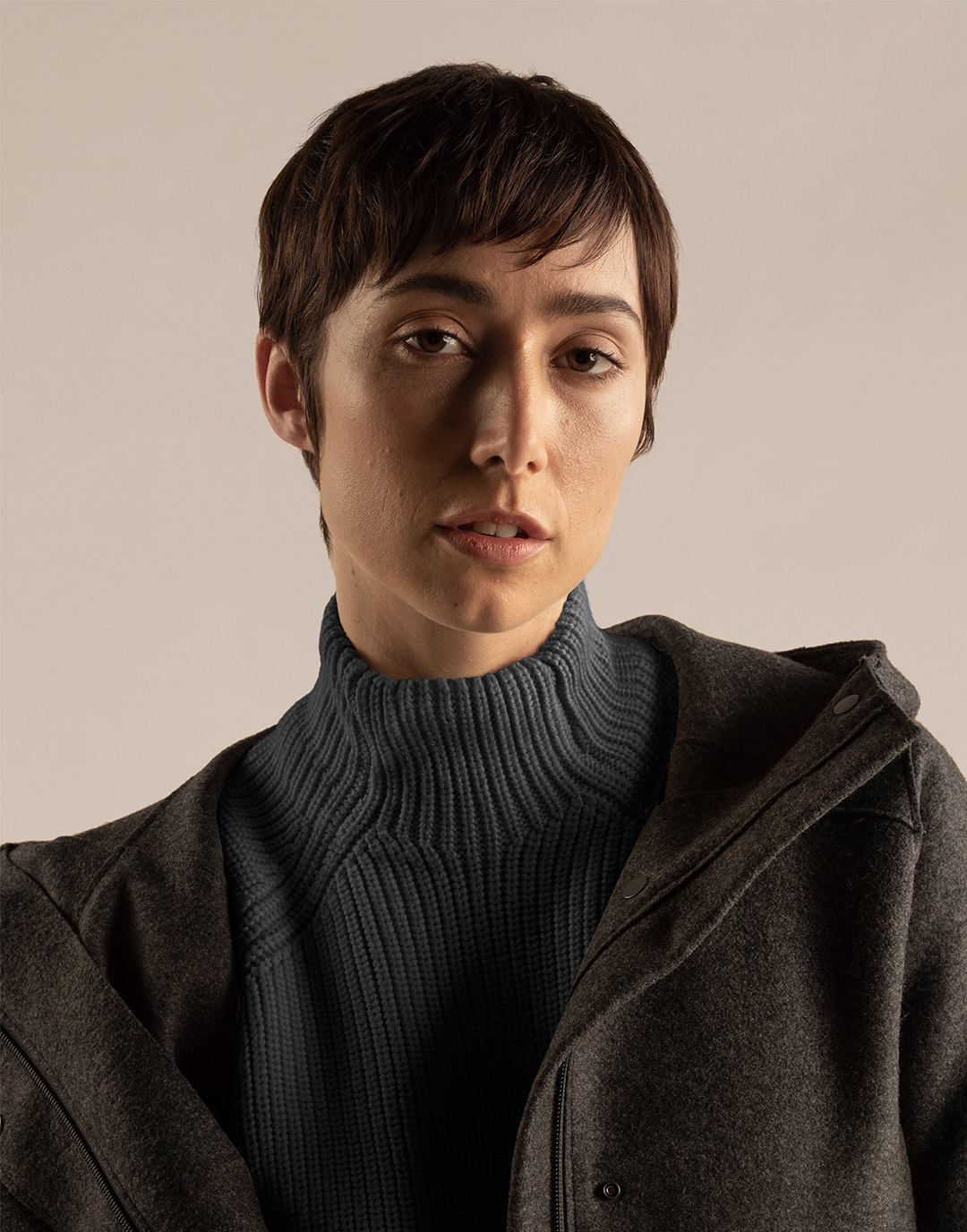 Een staande vrouw die een grijze jas en trui gemaakt van 100% merinowol draagt