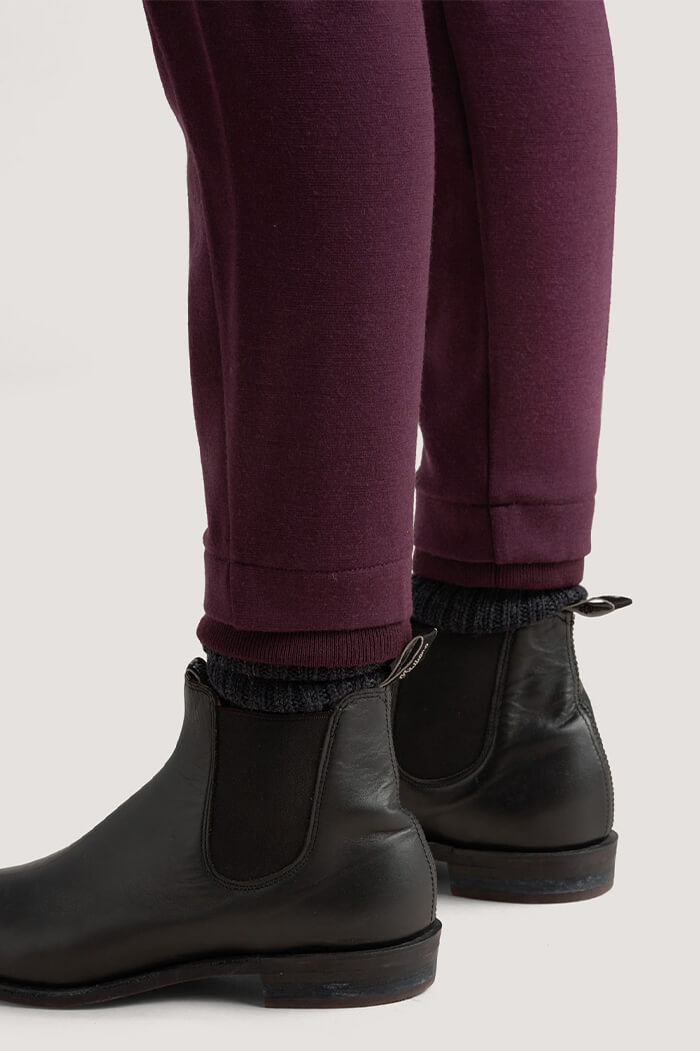 The hem of purple merino trousers, above a pair of black boots.