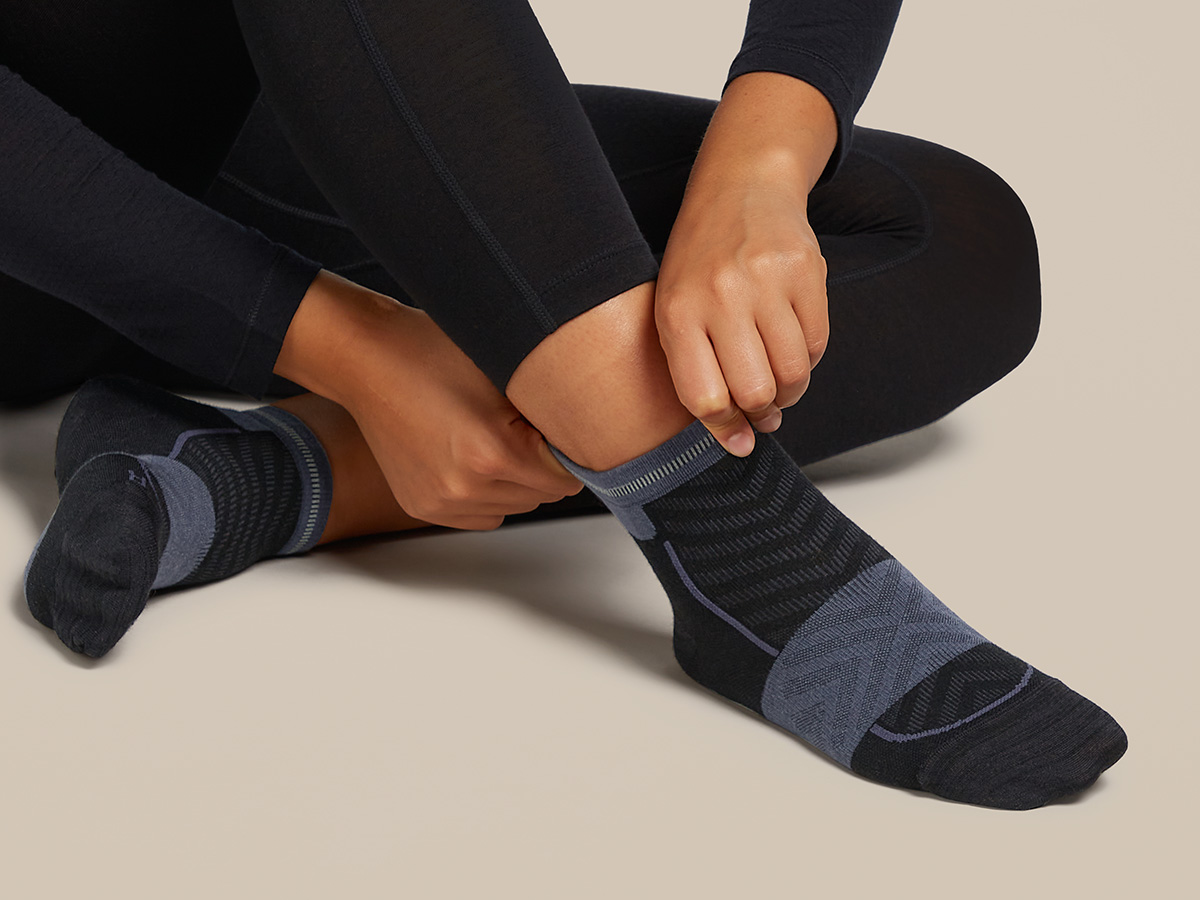Une femme enfile des chaussettes de course en mérinos Icebreaker