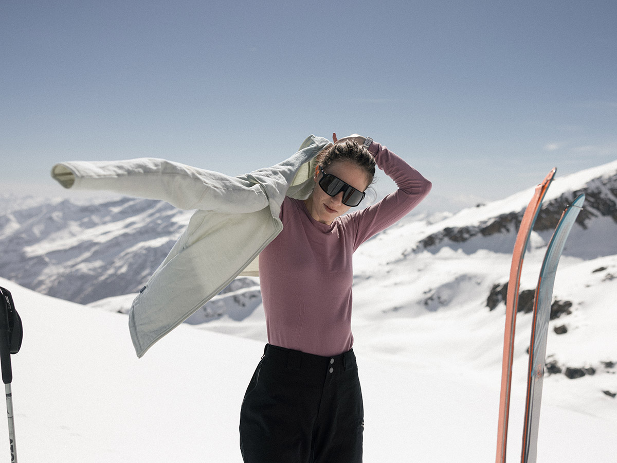 Une femme enfile un sweat-shirt par-dessus un haut thermique en mérinos